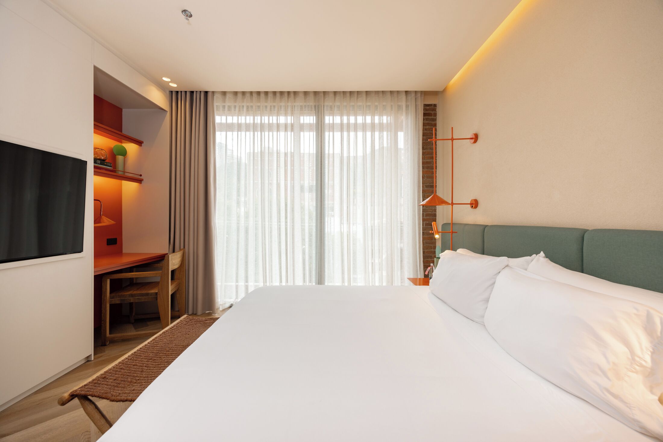 A hotel room with a large bed, a desk with a chair, a television, and a window with curtains.