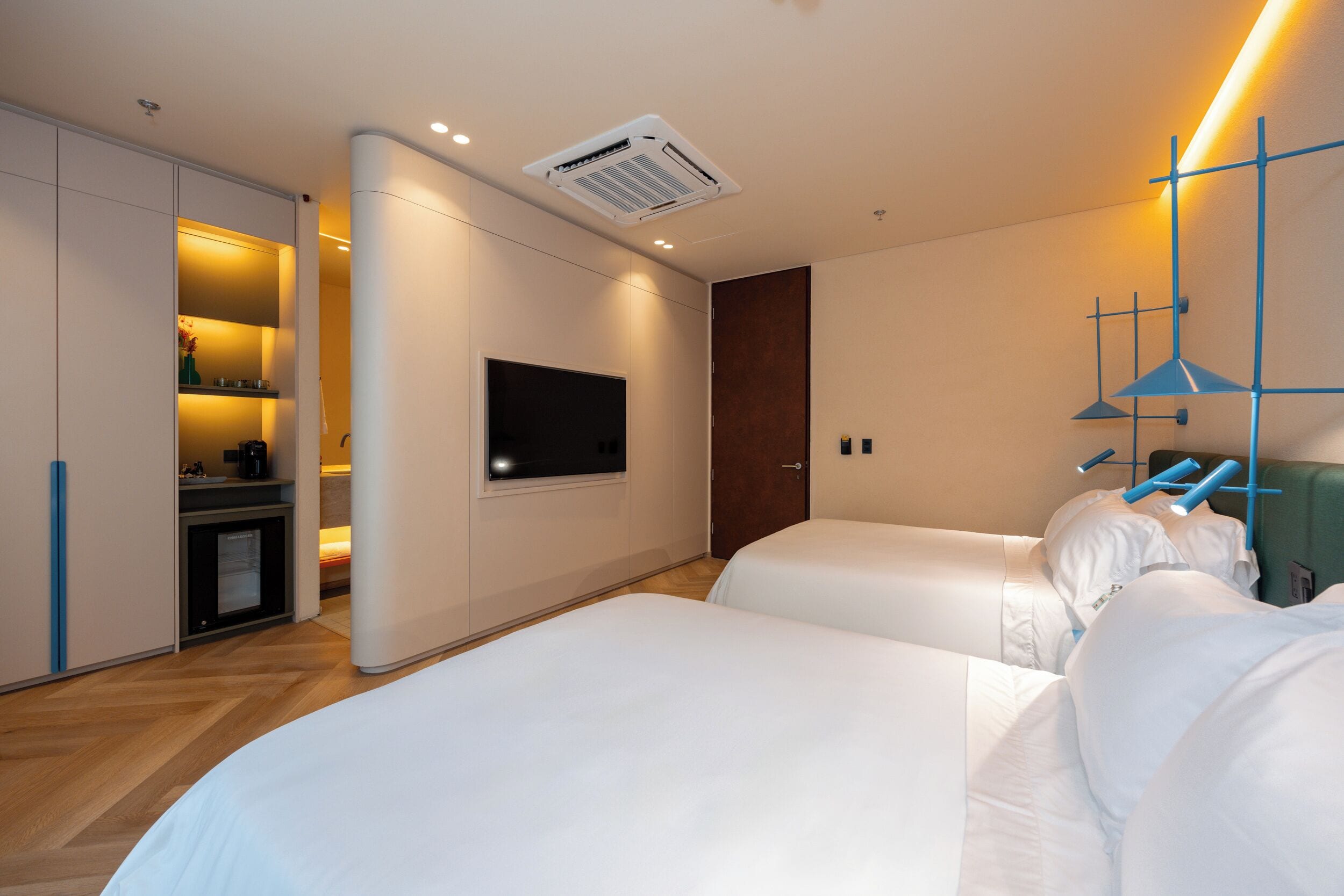 A hotel room with two beds, a television mounted on the wall, and a wardrobe with a mirror.