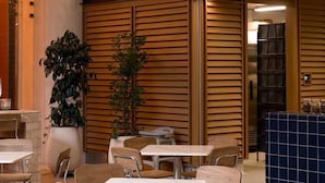 An indoor seating area with tables and chairs, a large sign reading 'PERGAMINO,' and a wooden wall design.