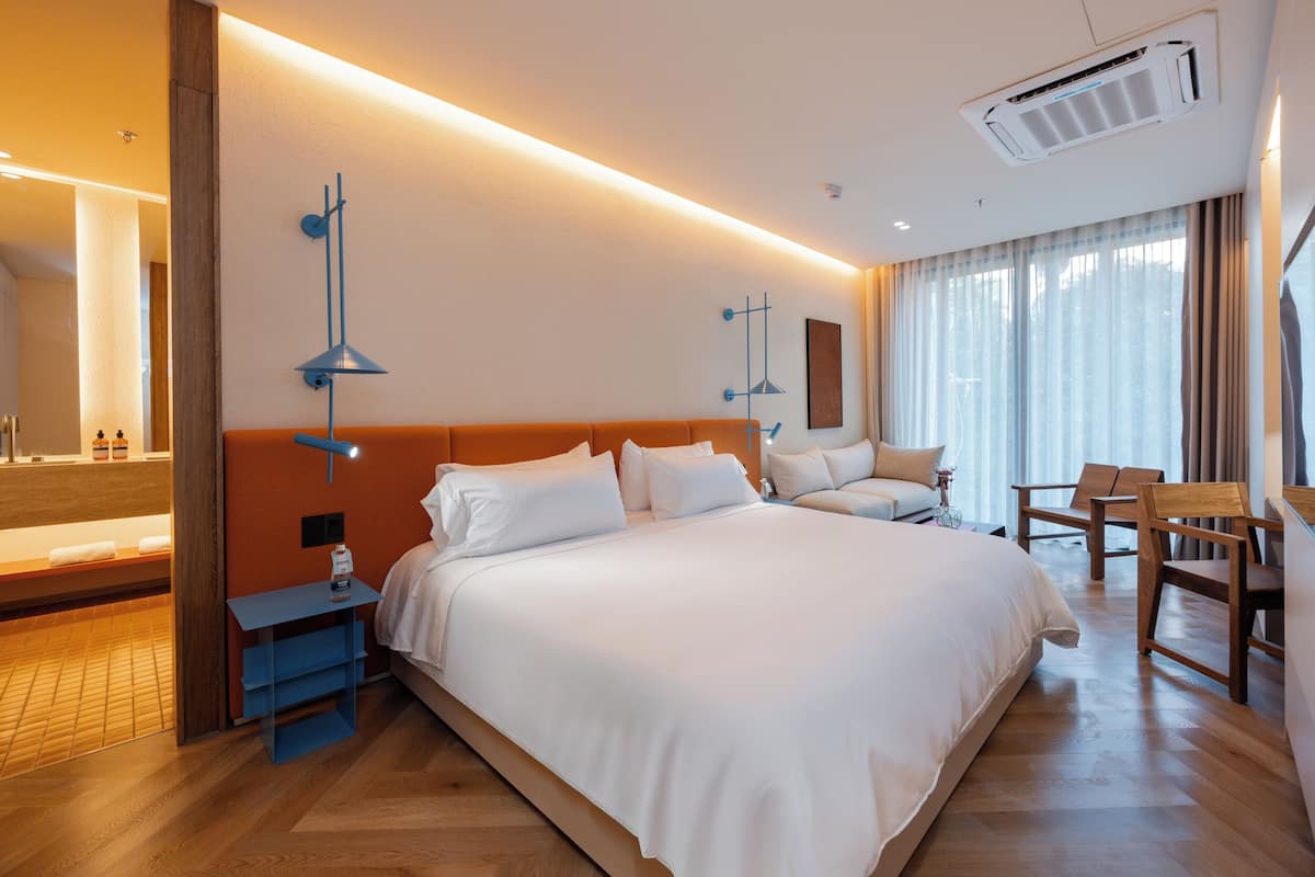 Quarto de hotel moderno com uma cama grande, mesas de cabeceira, uma escrivaninha e uma cadeira.