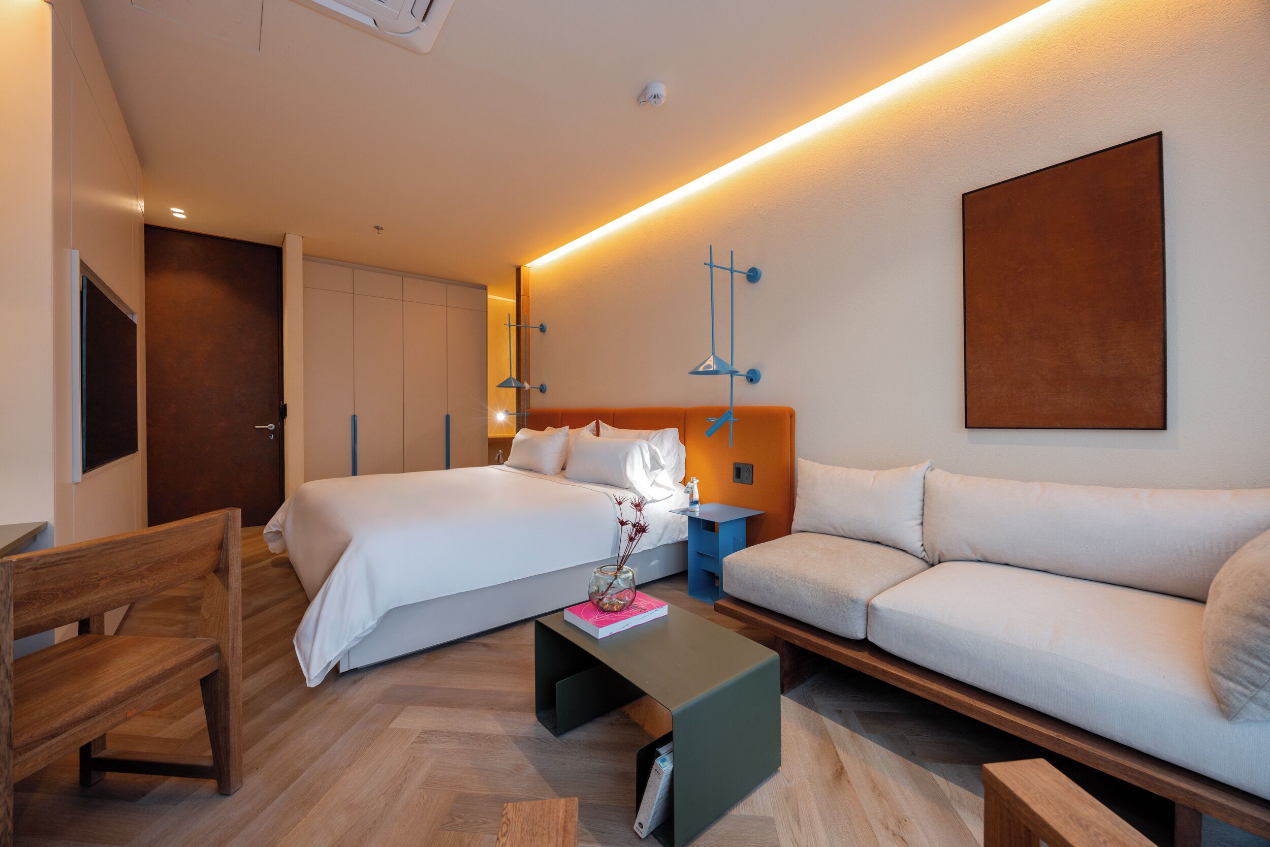 Une chambre d’hôtel moderne, dotée d’un grand lit, d’un canapé, d’un banc en bois et d’une petite table sur laquelle est posé un vase.