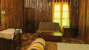 A rustic room with a wooden floor, a sofa, a small table with a chair, a bed, and a nightstand. - Amazing 4-Cabin "Bed & Breakfast" in Chimaltenango by Johnson (Chimaltenango)