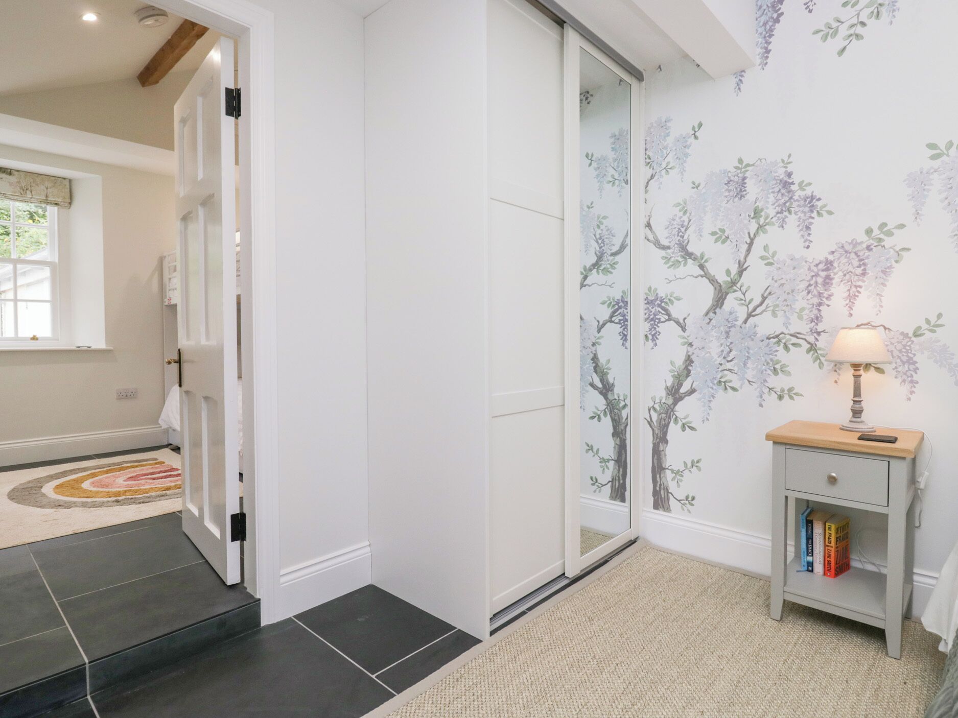 A hallway with a sliding door, a small bedside table with a lamp, and a bookshelf.