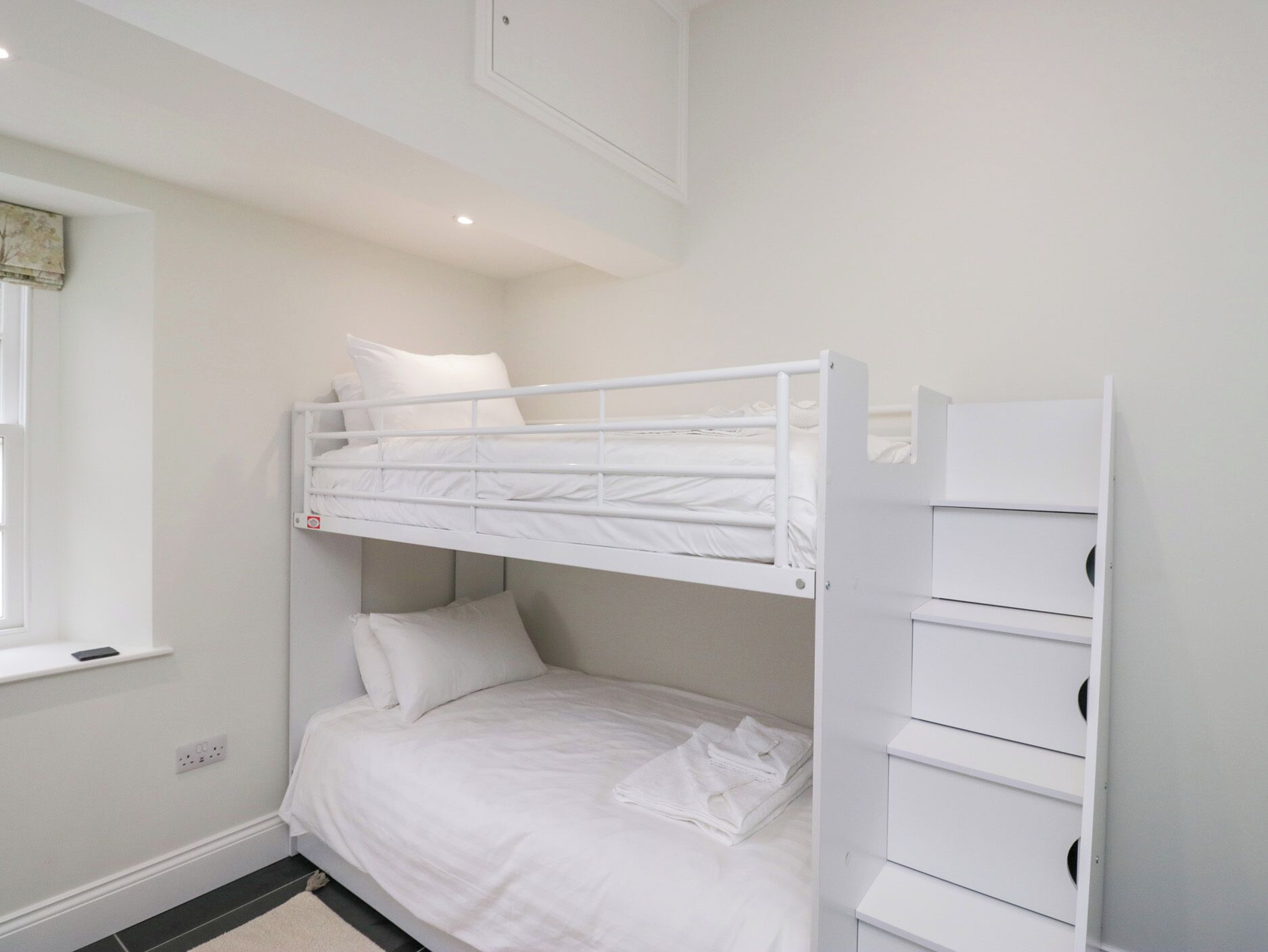 A bunk bed room with a white color scheme, a window, and a built-in storage unit.