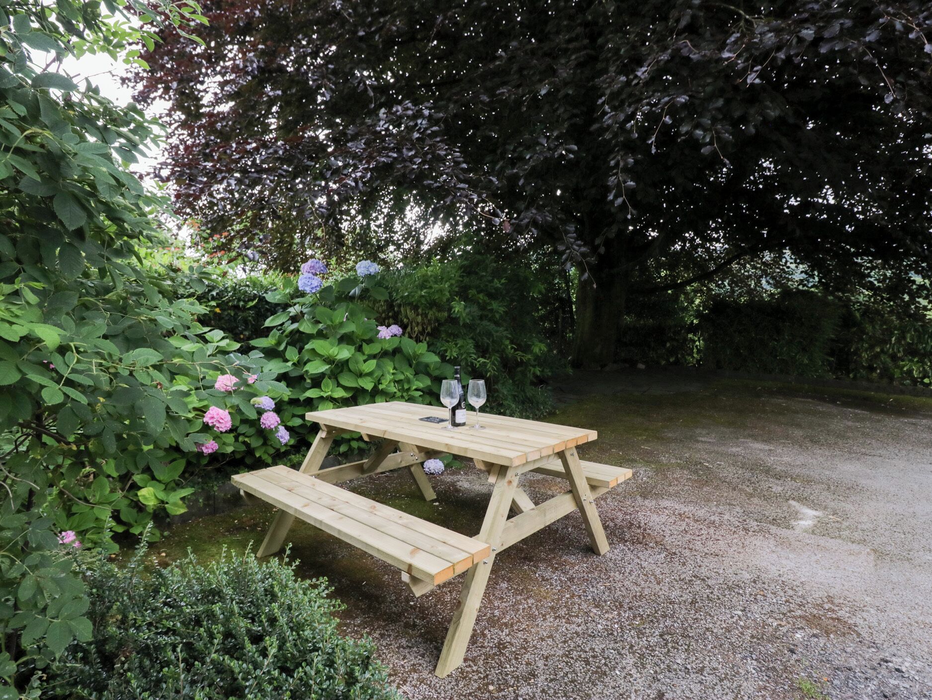 A wooden picnic table with benches, surrounded by lush greenery and flowering plants.