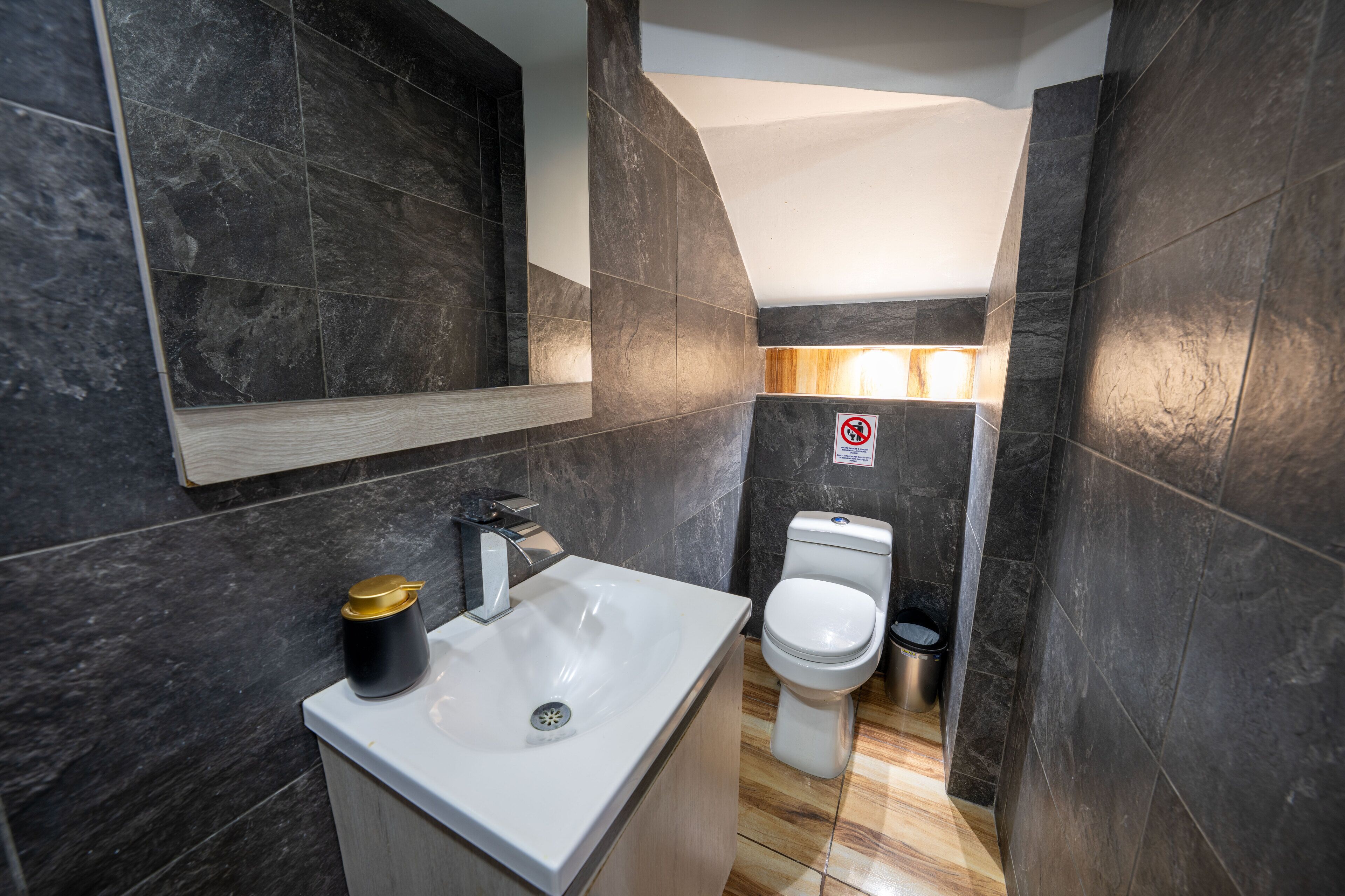 Une salle de bain moderne avec des murs recouverts de carreaux foncés, un lavabo blanc et des toilettes.