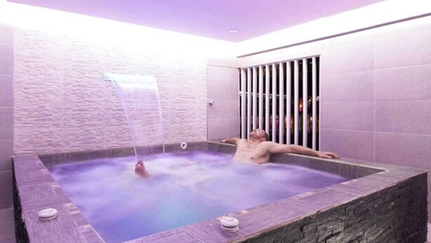 A man relaxing in a hot tub with a waterfall feature, surrounded by stone walls and a purple-lit ceiling. - Amazing 5 bedroom with Incredible Private Jacuzzi  1 block from LLeras (Medellín)