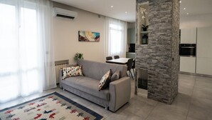 A modern living room with a grey sofa, a patterned rug, and a stone accent wall. - HouSmart Fiesso 9 (Castenaso)