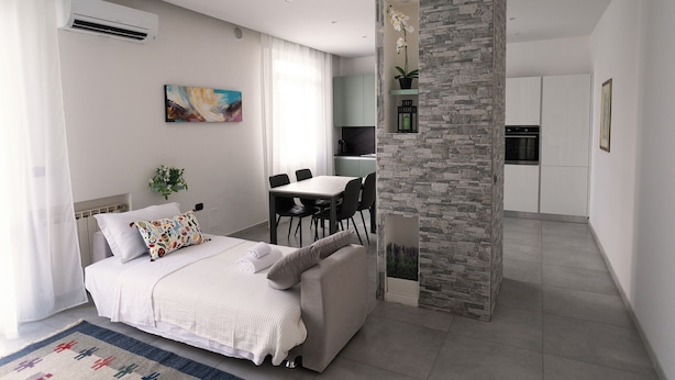 A modern bedroom with a bed, a dining table, and a kitchen area. - HouSmart Fiesso 9 (Castenaso)