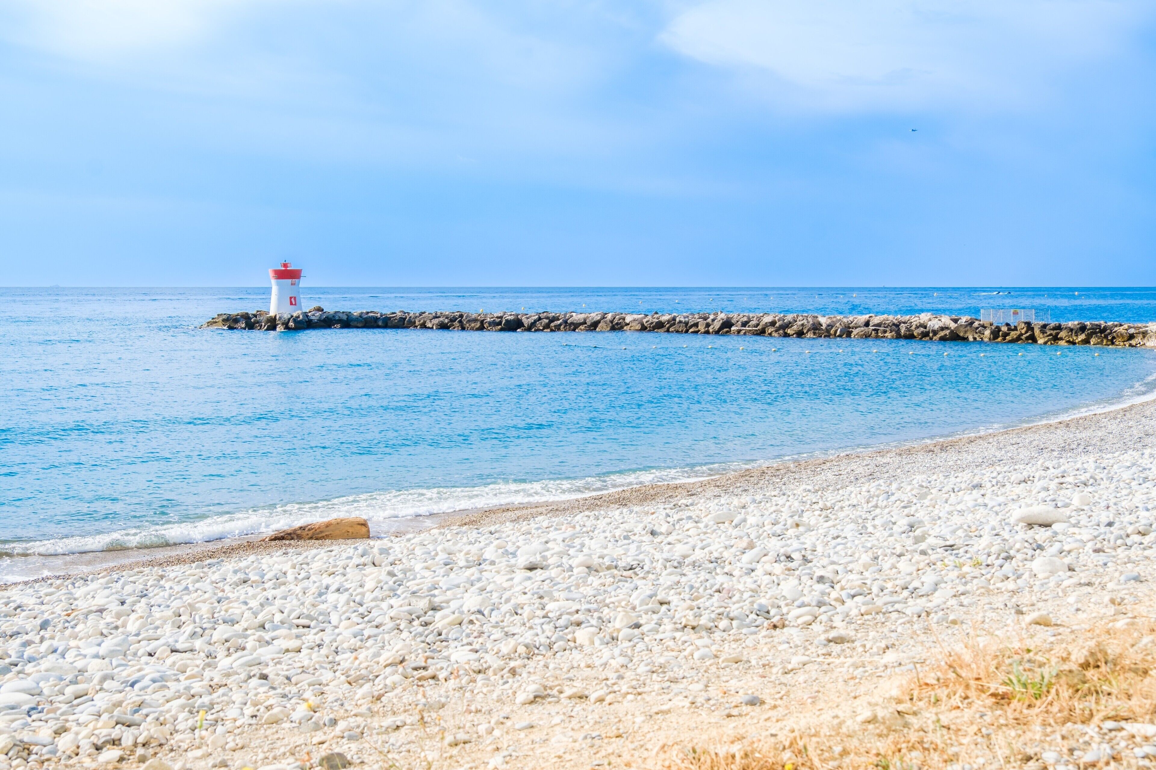 Een strand met een vuurtoren, een kiezelstrand en een rustige zee.