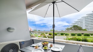 A balcony with a table set for two, an umbrella, and a view of a residential area.