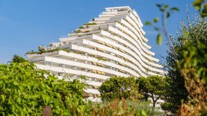 A modern multi-story building with balconies, surrounded by greenery.