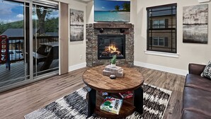 Un salon doté d’une cheminée en pierre, d’une table basse ronde et offrant une vue sur une terrasse aménagée avec du mobilier d’extérieur.