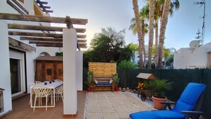 A patio with a table and chairs, a blue lounge chair, a wooden bench, and a small cart with plants. - Apartment in Vera playa. Between Sol and Salinas (AN)