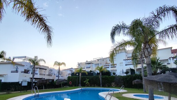 A pool area with a circular pool, surrounded by grass and palm trees, with modern buildings in the background. - Apartment in Vera playa. Between Sol and Salinas (AN)