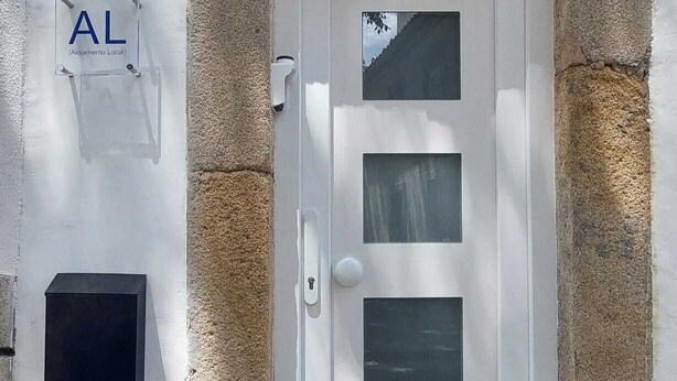 Une porte blanche encadrée de pierres, une boîte aux lettres et une enseigne indiquant « AL » et « Alojamento Local », ce qui signifie qu’il s’agit d’un hébergement local.