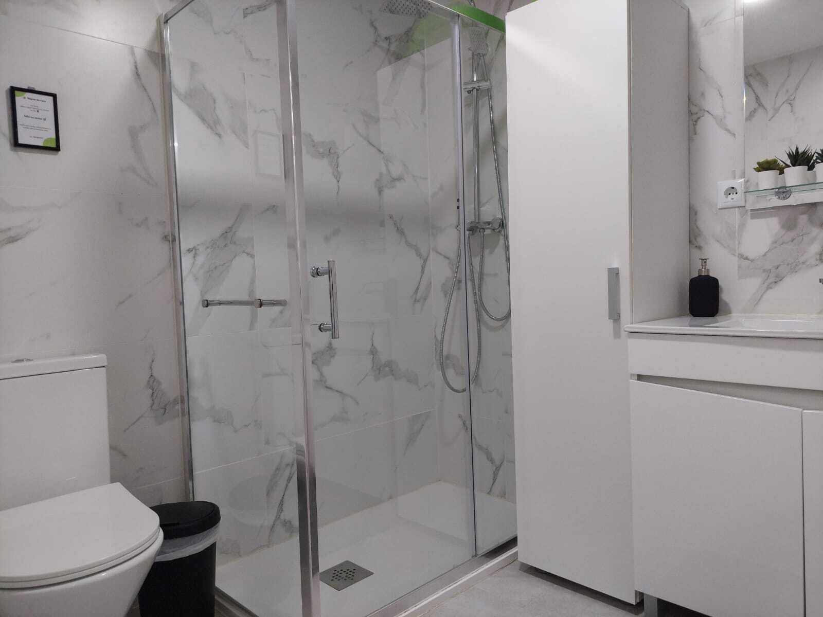 A bathroom with a glass-enclosed shower, a white toilet, and a marble-tiled wall.