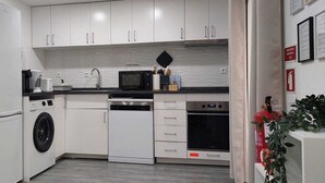 Une cuisine compacte avec des meubles blancs, un lave-linge, un four à micro-ondes et un lave-vaisselle.