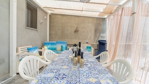 Un comedor con una mesa cubierta por un mantel azul y amarillo estampado, sillas blancas y un ventilador de techo.