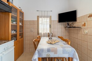 Ein Essbereich mit Tisch für zwei Personen, einem an der Wand befestigten Fernseher und einer Küche mit Holzausstattung und einem Herd.