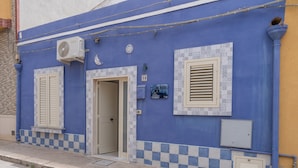 Un edificio con fachada azul, dos puertas y un ventanal con contraventanas.