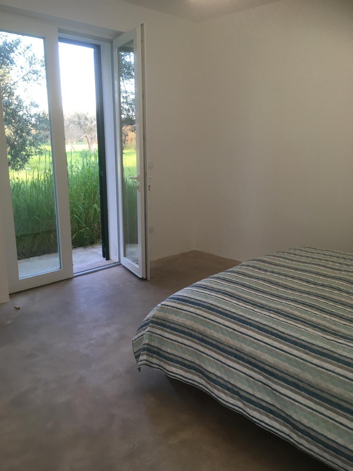 A bedroom with a bed, a sliding glass door leading to a balcony, and a view of a grassy area.