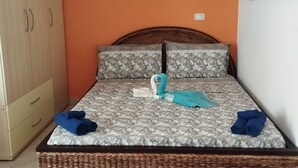 A bed with floral bedding, two pillows, a rolled towel, and a folded towel on a wicker bed frame.