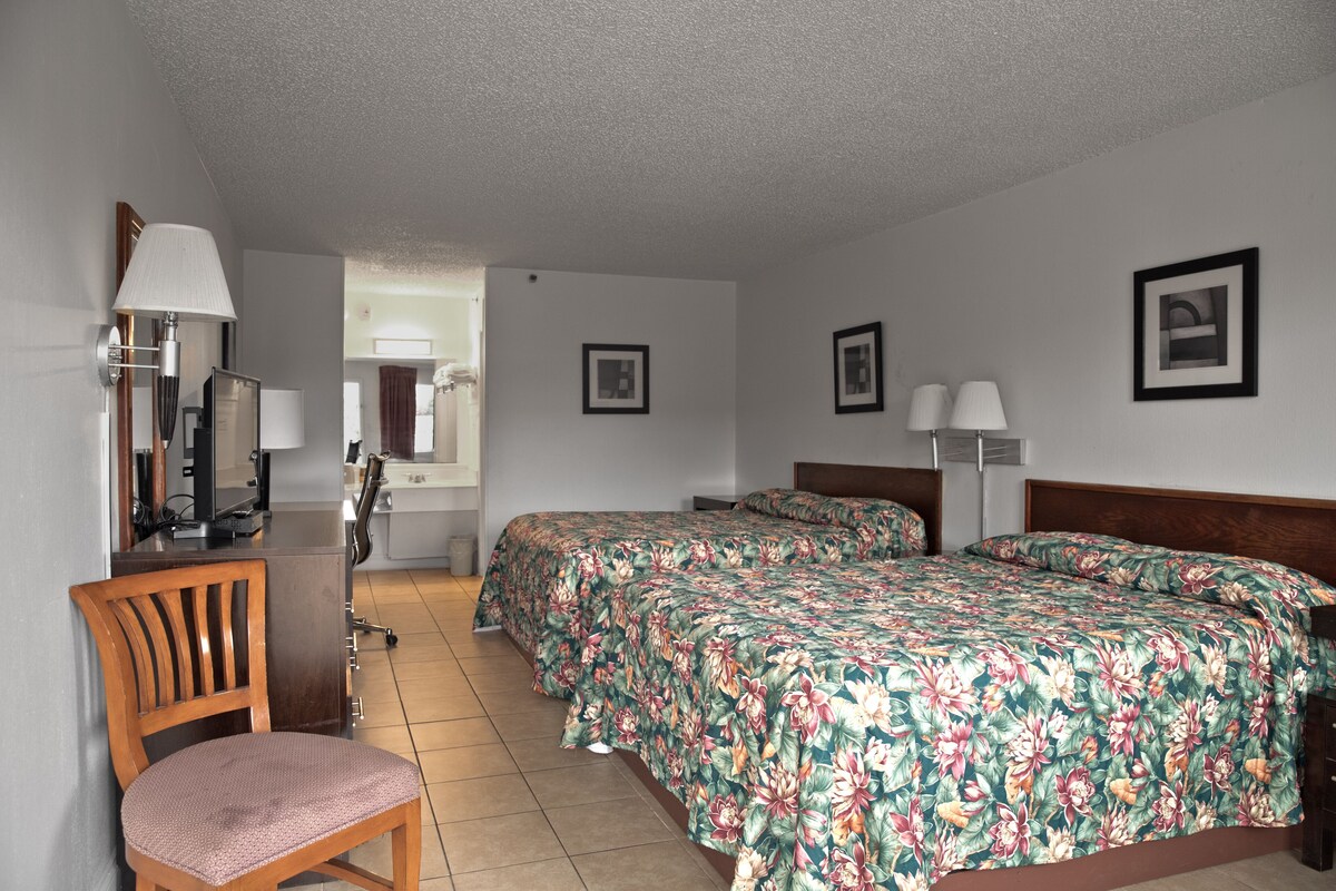 A hotel room with a bed, two bedside tables, a chair, a desk with a lamp, and a mirror.
