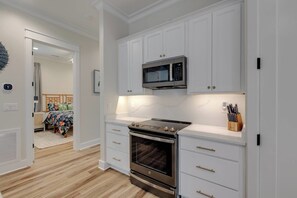 A compact kitchen with white cabinets, a microwave, an oven, and a countertop with a knife block. - Mari Muria Beach House (Orange Beach)