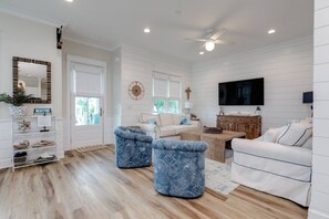 A spacious living room with a white sofa, blue ottomans, a wooden coffee table, and a flat-screen TV mounted on the wall. - Mari Muria Beach House (Orange Beach)