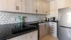 Una cucina moderna con mobili chiari in legno, un piano di lavoro in granito nero, elettrodomestici in acciaio inossidabile e una parete backsplash rivestita in piastrelle.