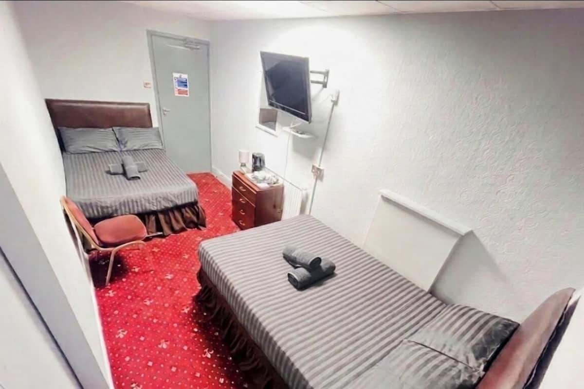 A hotel room with two beds, a TV, a dresser, and a red carpet.