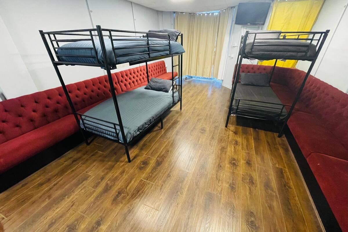 A room with bunk beds, a red sofa, and a wooden floor.