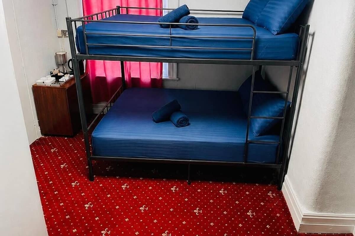 A bunk bed room with a red patterned carpet, a small wooden nightstand, and a window with pink curtains.