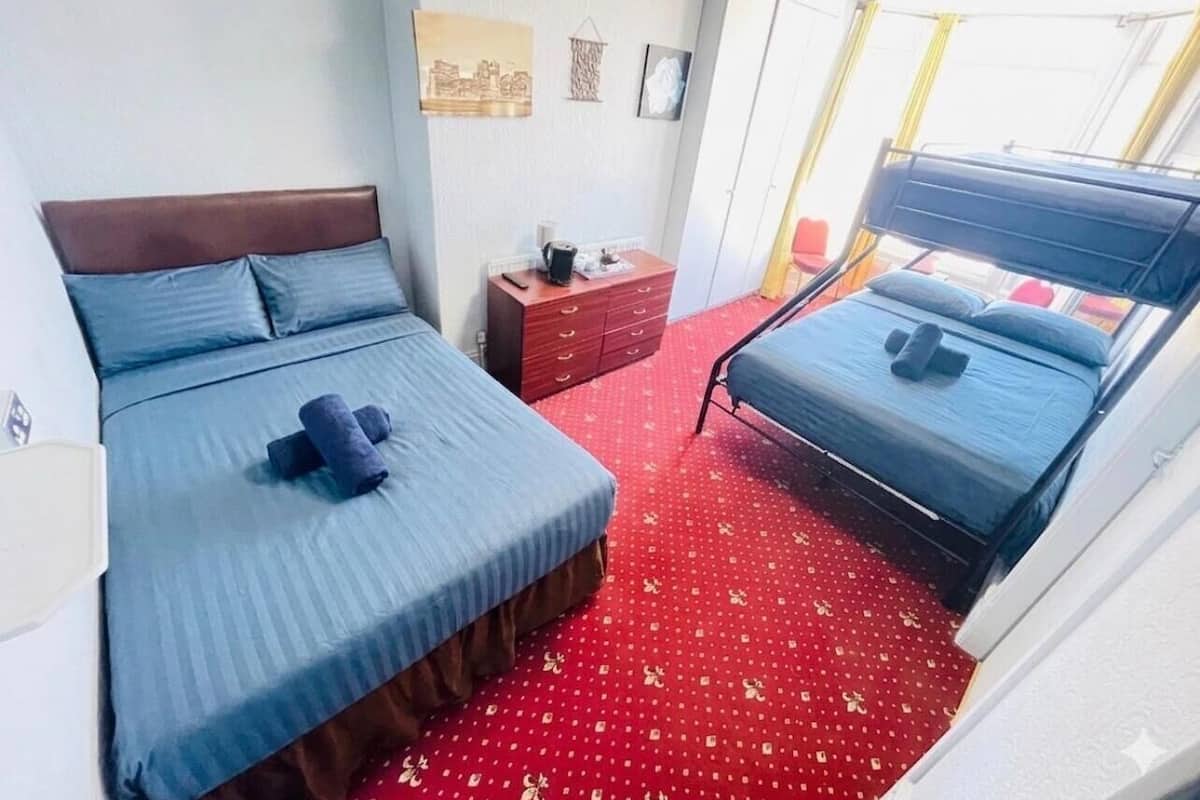 A hotel room with two beds, a red carpet, a wooden dresser, and a window with curtains.