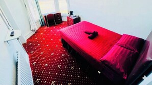 Una habitación con cama, una silla, una mesita y una ventana con cortinas.