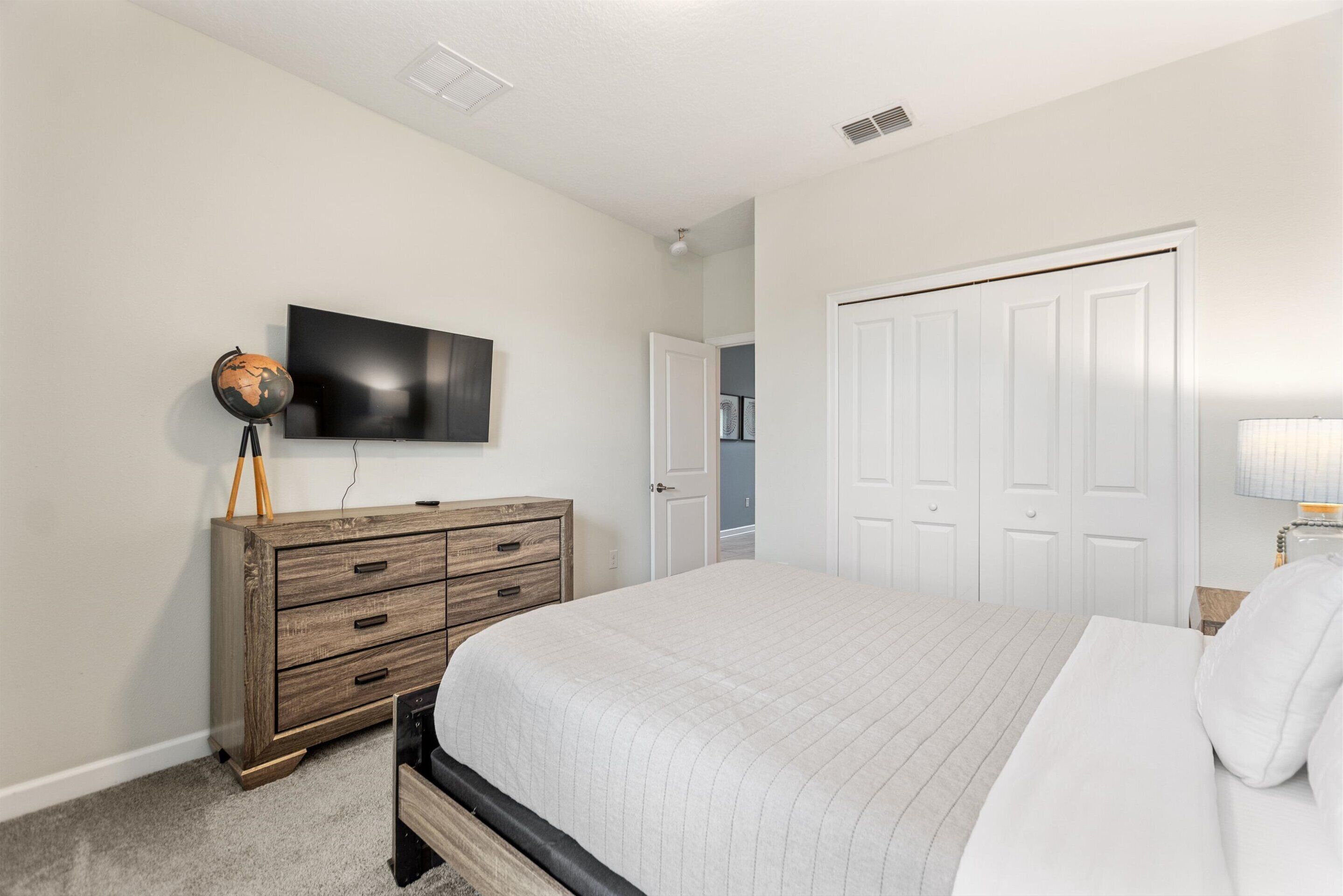 A bedroom with a bed, a dresser, a TV, and a door.