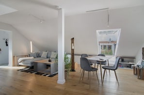 A modern loft with a dining area, a sofa, and a large window.