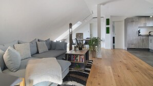 Un loft moderno con techo alto, un sofá gris, una estantería y una zona de cocina.