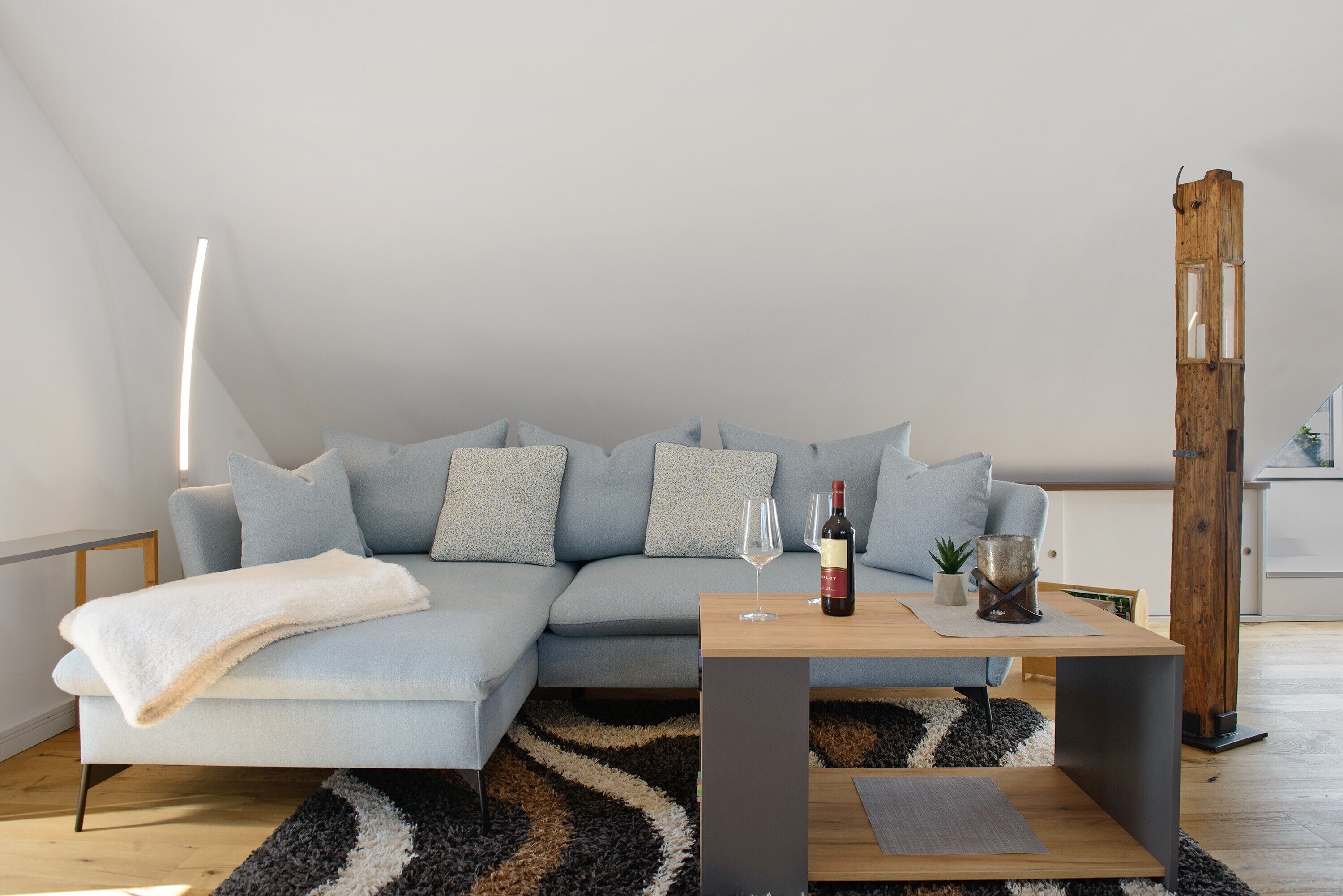 Ein modernes Wohnzimmer mit einem hellblauen Sofa, einem Holztisch, einem schwarz-weißen Teppich und einer hohen Holzsäule.