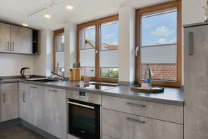 A modern kitchen with a built-in oven, stainless steel appliances, and large windows.