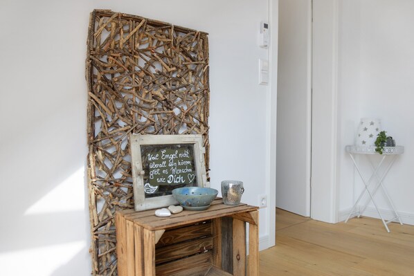 A rustic wall decor with a chalkboard sign, a wooden table with a bowl and a cup, and a small plant on a white stand.