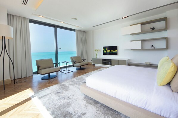 Una habitación de hotel moderna con una cama grande, televisión, escritorio y vista al mar.