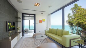 Una sala de estar moderna con un ventanal que da al mar, un sofá verde y una mesa de centro de vidrio.