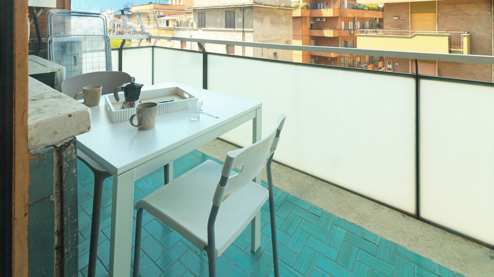 Een balkon met een witte tafel en stoelen, een waterkoker en een mok.