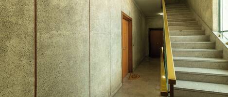 A hallway with a concrete wall, a wooden door, and a staircase with a metal handrail.
