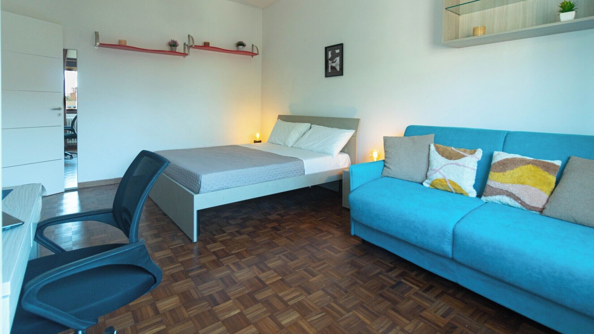 Ein Schlafzimmer mit Bett, Schreibtisch, Stuhl, blauem Sofa und Holzboden mit Fischgrätmuster.