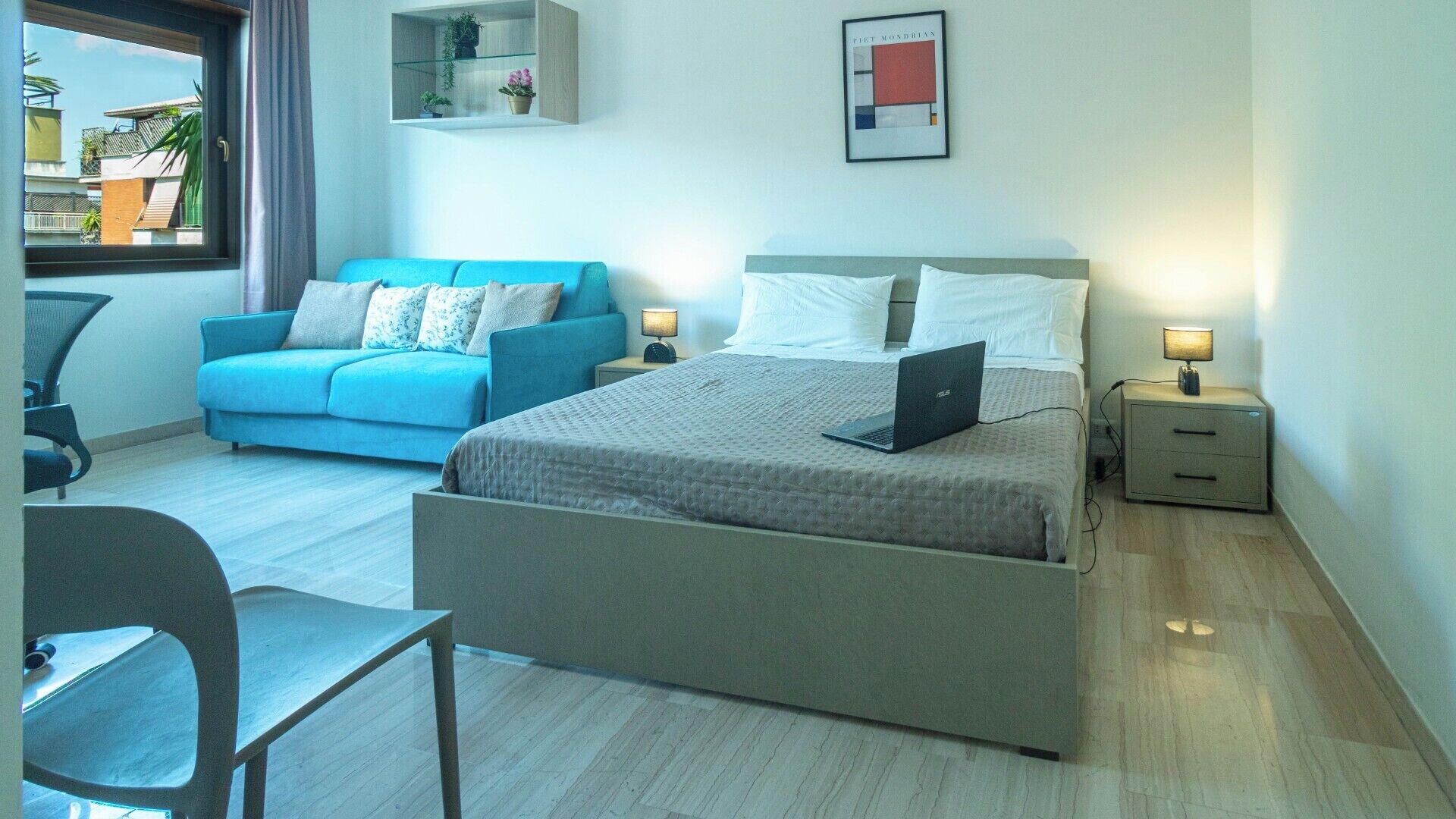 Ein modernes Hotelzimmer mit einem Bett, einem Schreibtisch, einem blauen Sofa und einem Nachttisch mit Lampe.