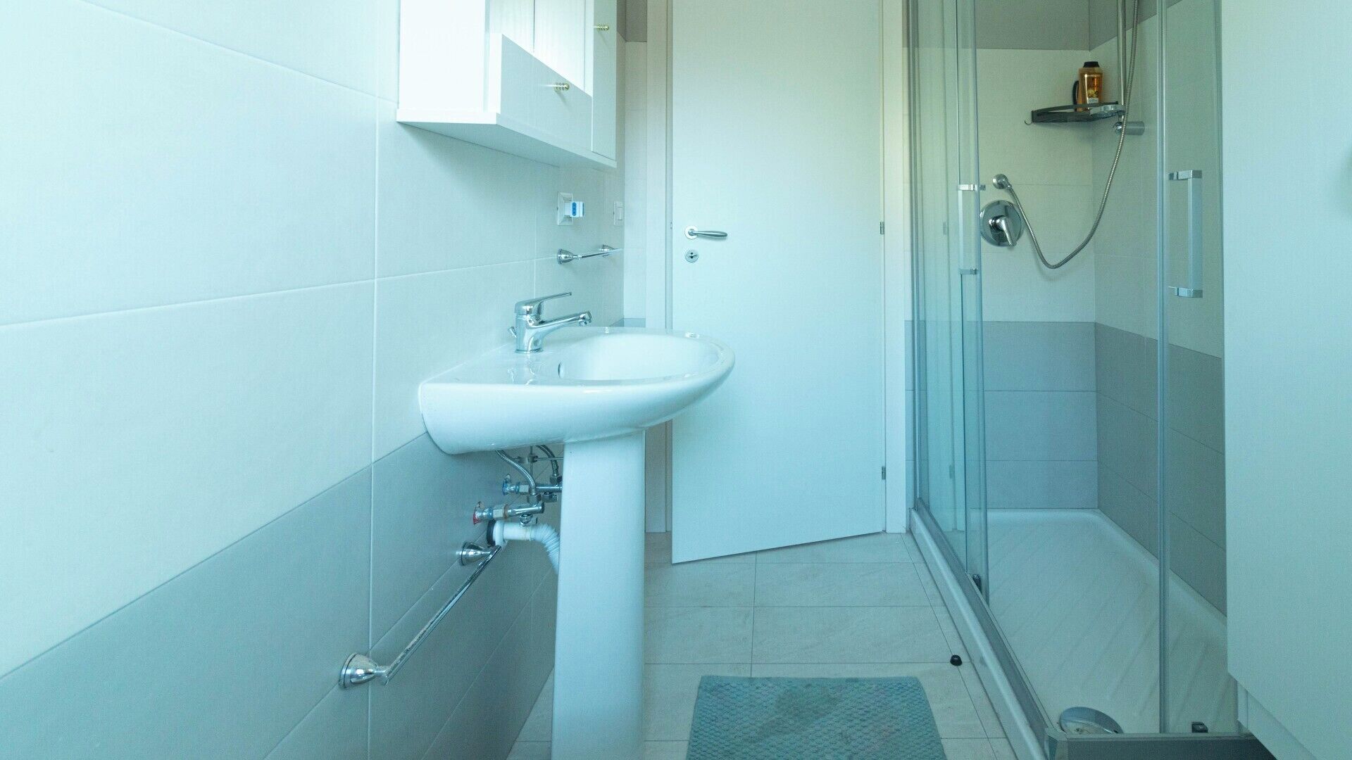 A bathroom with a white sink, a glass shower enclosure, and a tiled floor.