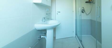 A bathroom with a white sink, a glass shower enclosure, and a tiled floor.